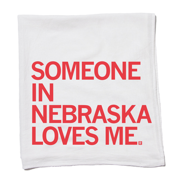 A flour sack towel made of white fabric with the red text, SOMEONE IN NEBRASKA LOVES ME.