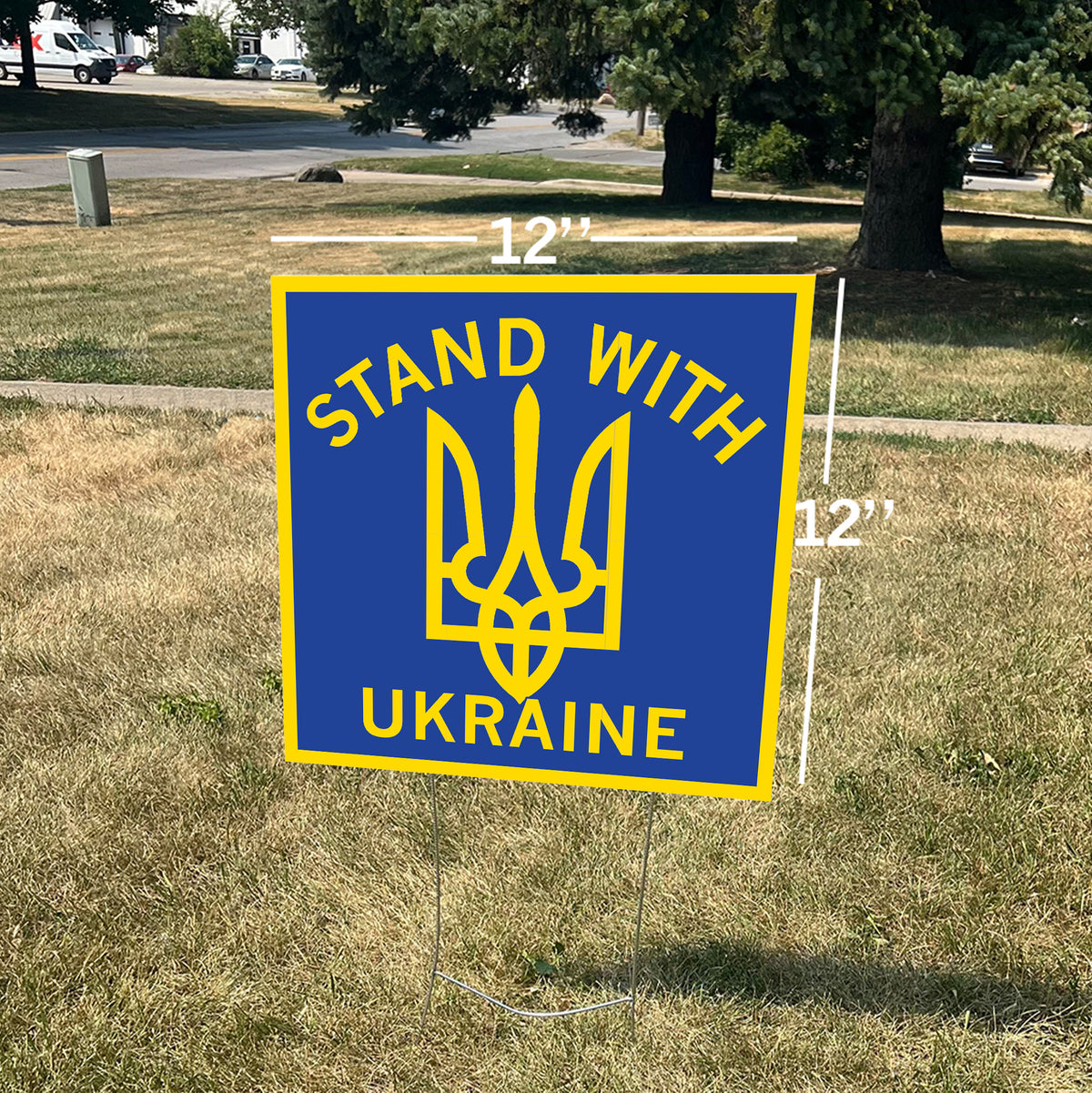 A 12-inch square Stand With Ukraine yard sign featuring a yellow Ukrainian trident symbol on a lawn.