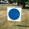 A 12-inch by 12-inch square RAYGUN yard sign featuring a large blue circle with a white outline of Nebraska and the text THE BLUE DOT.