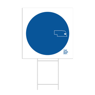 A yard sign featuring a large blue circle containing an outline of Nebraska, with the text THE BLUE DOT. below the map, representing the Omaha Blue Dot movement.