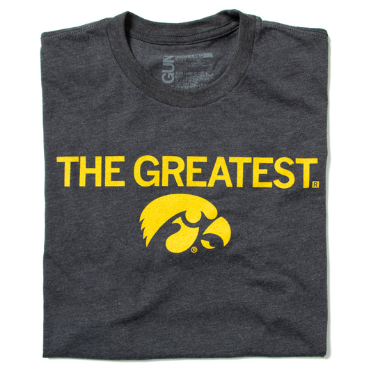 Charcoal grey, officially licensed Iowa Hawkeyes t-shirt featuring THE GREATEST printed in yellow above a yellow Tigerhawk logo.