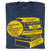 A union made, heather denim t-shirt featuring a yellow graphic of a book stack with titles of frequently challenged books and a starburst warning label that reads, Warning: Too dangerous to read! Open with extreme caution.