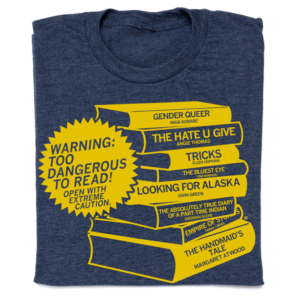A union made, heather denim t-shirt featuring a yellow graphic of a book stack with titles of frequently challenged books and a starburst warning label that reads, Warning: Too dangerous to read! Open with extreme caution.