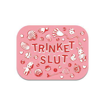 A rectangular pink RAYGUN vinyl sticker with the text TRINKET SLUT surrounded by illustrations of small objects including a doll, a die, a key, a toy rabbit, and a bottle cap.