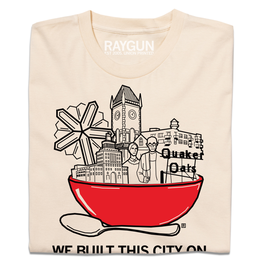 Cream-colored RAYGUN t-shirt featuring a graphic of a large red bowl filled with buildings and a Quaker Oats logo, with the text WE BUILT THIS CITY ON below.