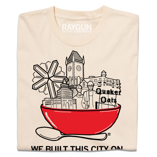 Cream-colored RAYGUN t-shirt featuring a graphic of a large red bowl filled with buildings and a Quaker Oats logo, with the text WE BUILT THIS CITY ON below.