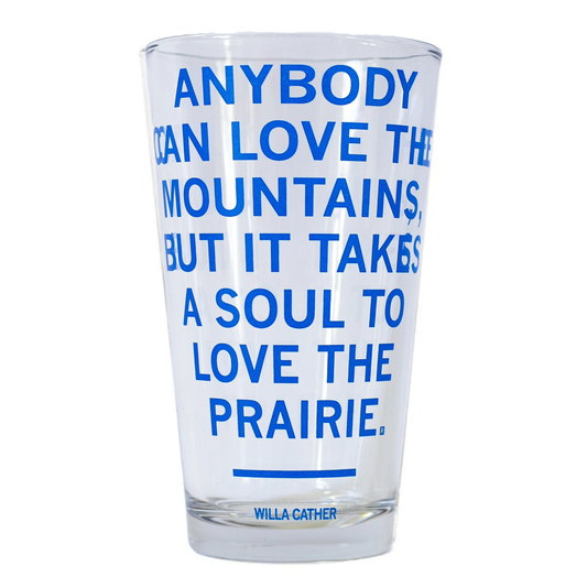 A dishwasher-safe pint glass featuring blue text that reads, Anybody can love the mountains, but it takes a soul to love the prairie, with Willa Cather written at the bottom.