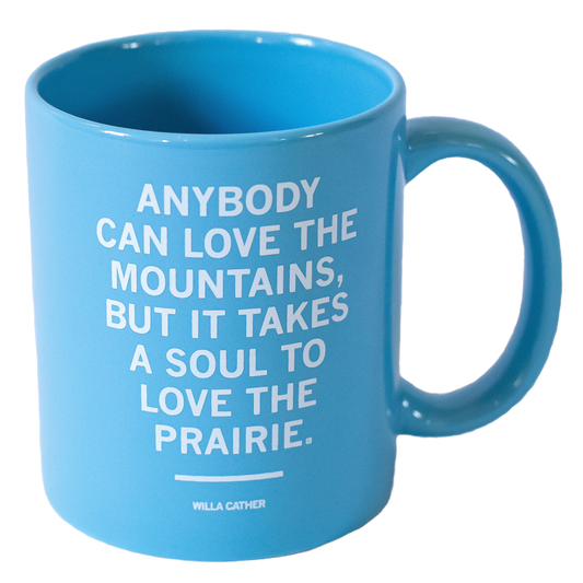Light blue dishwasher safe mug featuring the Willa Cather quote: ANYBODY CAN LOVE THE MOUNTAINS, BUT IT TAKES A SOUL TO LOVE THE PRAIRIE.