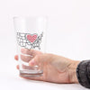 A hand holds a dishwasher-safe Midwest pint glass featuring a black outline of the United States with a red heart icon over the center.
