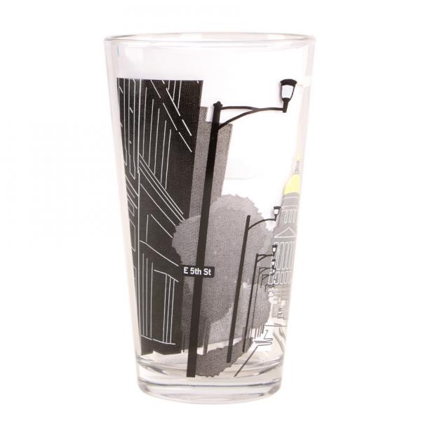 A clear, American-made pint glass decorated with a black-and-white city street scene that includes a street sign reading E 5th St.