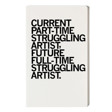 A white, screen-printed notebook with black text that reads, CURRENT PART-TIME STRUGGLING ARTIST, FUTURE FULL-TIME STRUGGLING ARTIST.