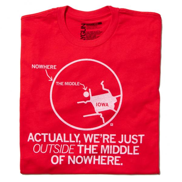 Red Iowa t-shirt featuring a map of the state inside a circle labeled The Middle with an arrow from Nowhere, and the text Actually, were just outside the middle of nowhere printed below; a retired design.