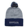 Grey knit beanie with a navy blue folded cuff featuring RAYGUN embroidered in white text and a navy and grey pom-pom on top.