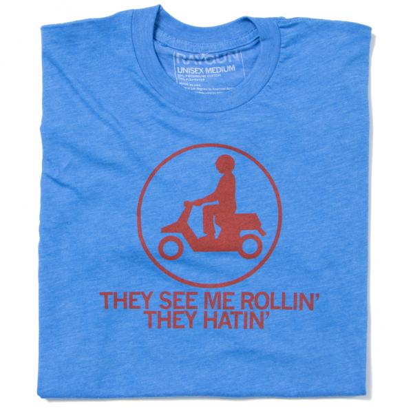 Blue Raygun t-shirt featuring a red icon of a person riding a scooter inside a circle, with the text THEY SEE ME ROLLIN THEY HATIN printed below.