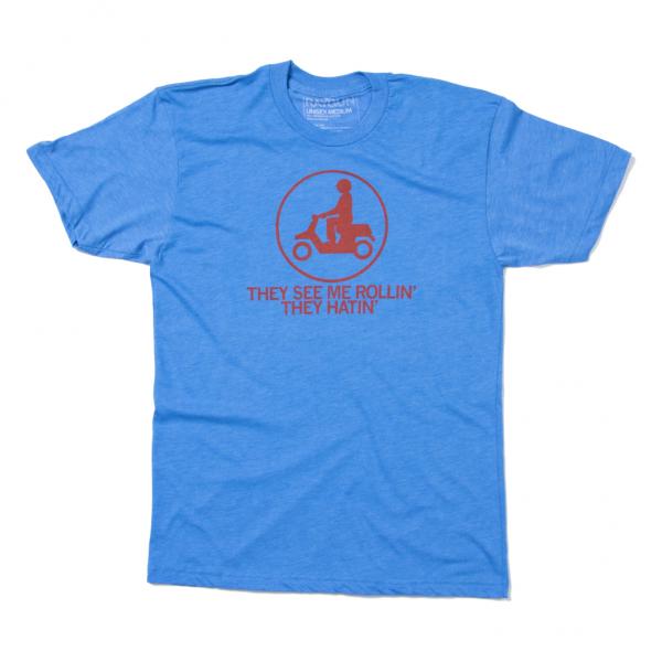 Blue Raygun t-shirt featuring a red icon of a person on a scooter inside a circle, with the text THEY SEE ME ROLLIN THEY HATIN below it.