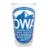 A clear Iowa pint glass featuring a blue graphic of mountains and the text IOWA: THE ANSWER TO LIFES ETERNAL QUESTION: WHOS DRINKING SO MUCH BUSCH LIGHT?!?!.