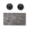 The back of a rectangular RAYGUN enamel pin with two metal posts and two black rubber pin backs.
