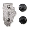 The back of an Illinois Gay Pride enamel pin shaped like the state, with two black rubber pin backs to the right.