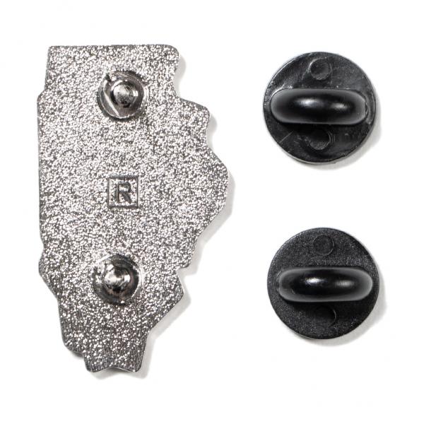 The back of an Illinois Gay Pride enamel pin shaped like the state, with two black rubber pin backs to the right.