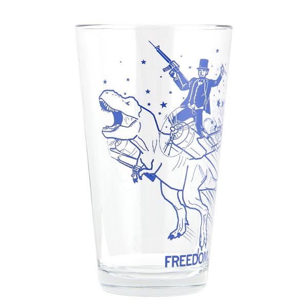 Clear pint glass with a blue illustration of Abraham Lincoln riding a T-Rex while holding a rifle, with the word FREEDOM printed at the base.