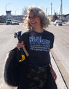 A smiling woman wears an inspirational RAYGUN t-shirt that says Be Like Fleur Drive: Never stop working on yourself, no matter how inconvenient it is for everyone else while holding a yellow crowbar.