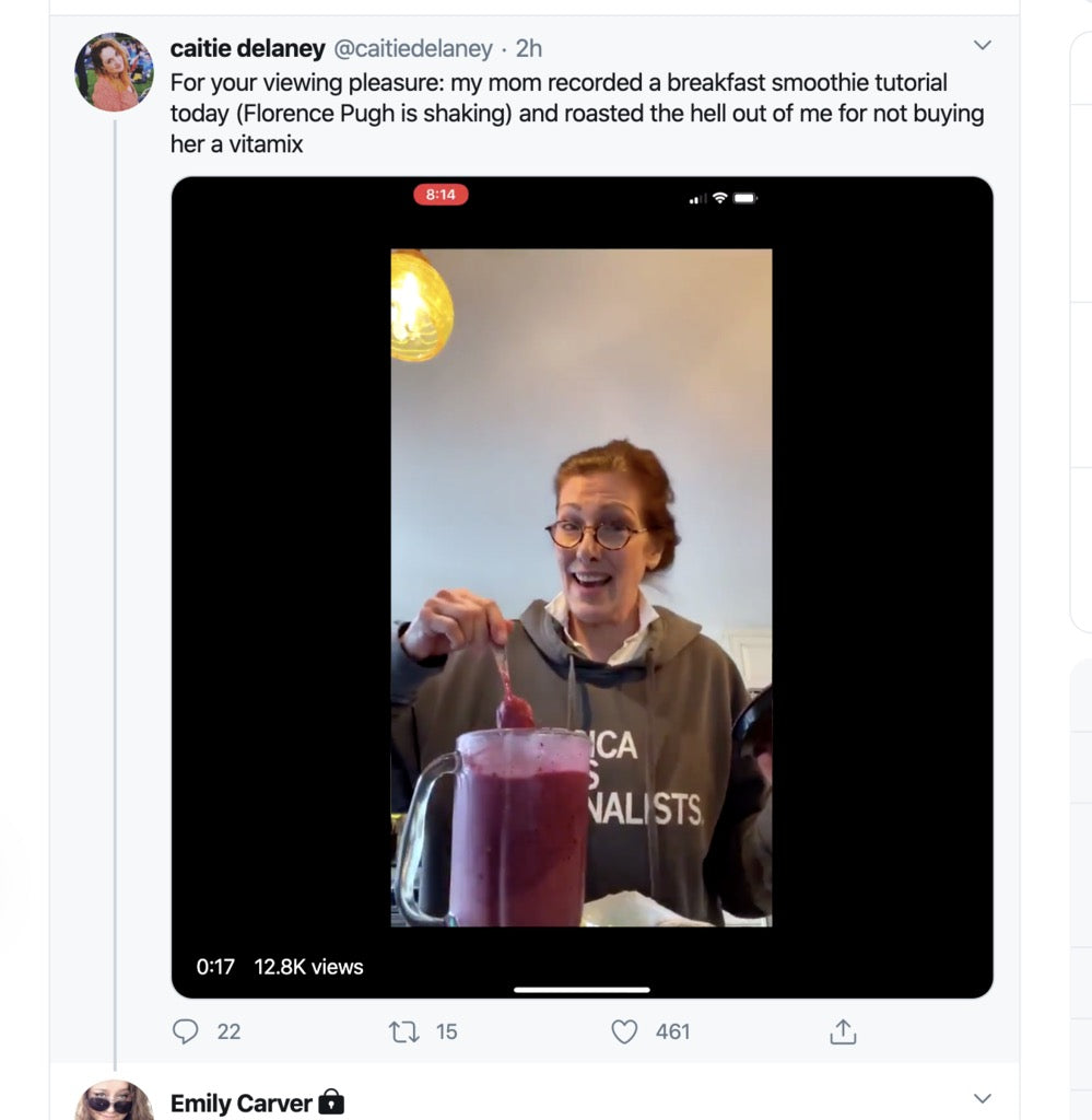 A woman in a Pigment Black Pullover Hoodie speaks to the camera while stirring a large pitcher of purple smoothie.