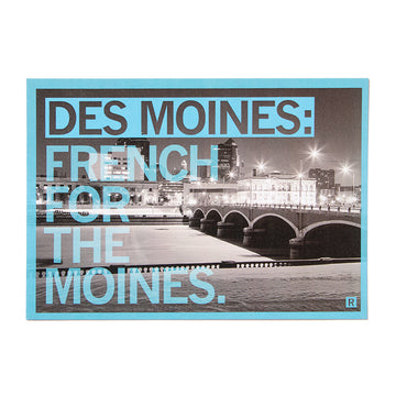A black-and-white RAYGUN postcard featuring a night view of the Des Moines riverfront with the text DES MOINES: FRENCH FOR THE MOINES. overlaid in large light blue letters.
