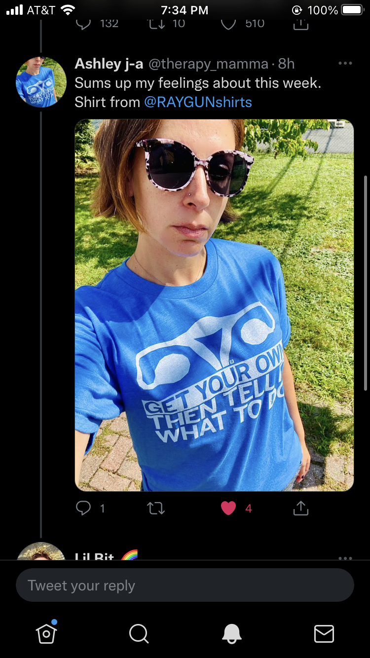A person wearing patterned sunglasses and a sweatshop-free, bright blue t-shirt that says Get your own then tell me what to do.