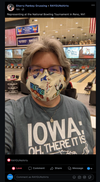 A person wearing glasses and a bowling-themed face mask stands in a bowling alley, wearing a gray Iowa t-shirt that says IOWA: OH, THERE IT IS.