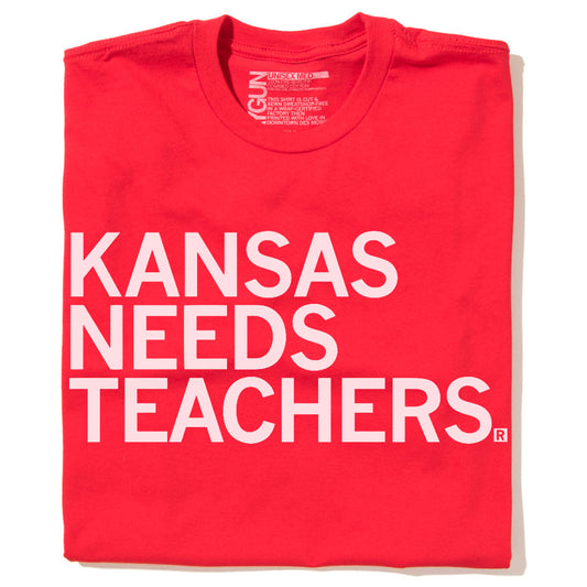 A red Kansas Needs Teachers t-shirt with the text printed in large white capital letters.