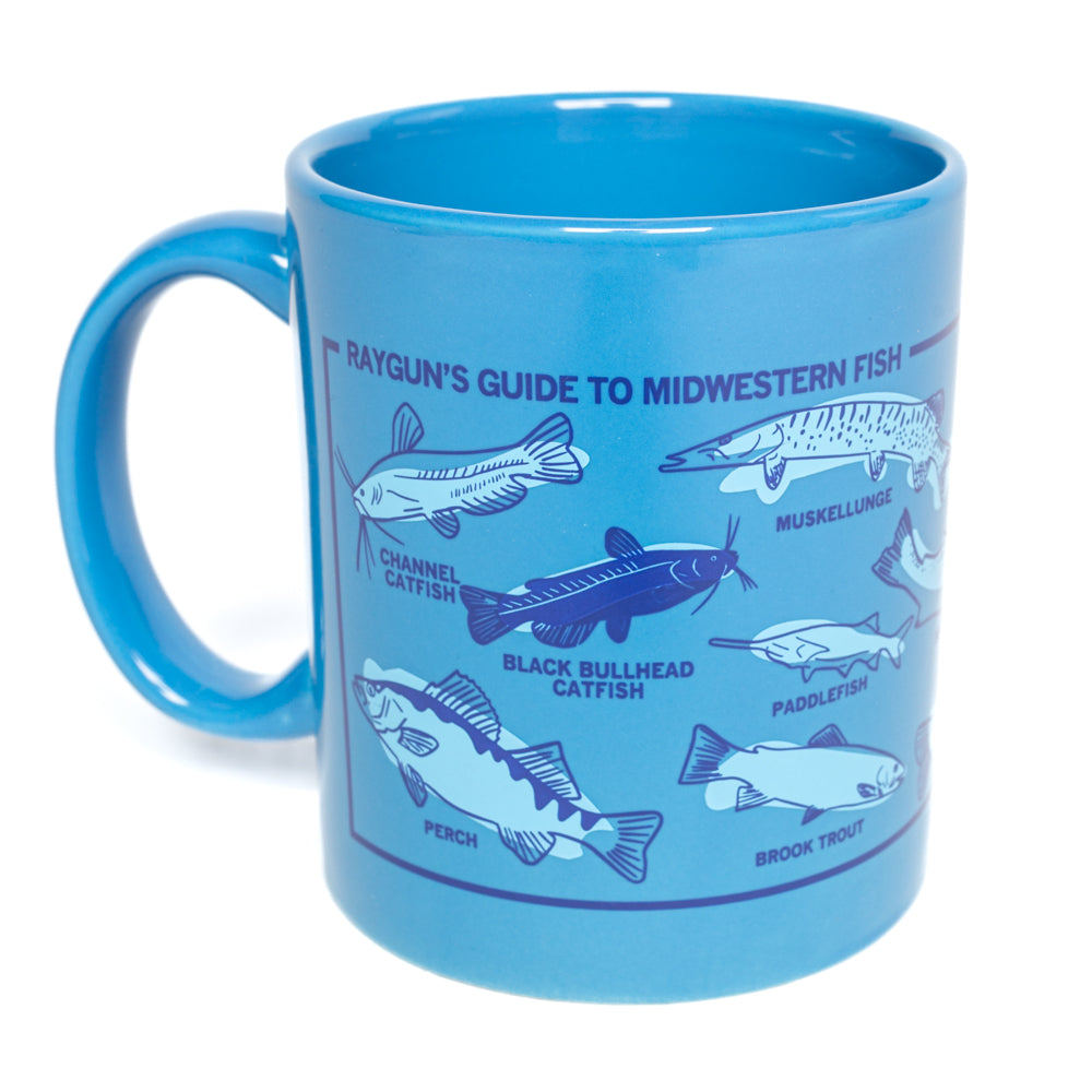 A bright blue RAYGUN mug printed with a Rayguns Guide to Midwestern Fish, featuring labeled illustrations of channel catfish, black bullhead catfish, muskellunge, paddlefish, perch, and brook trout.