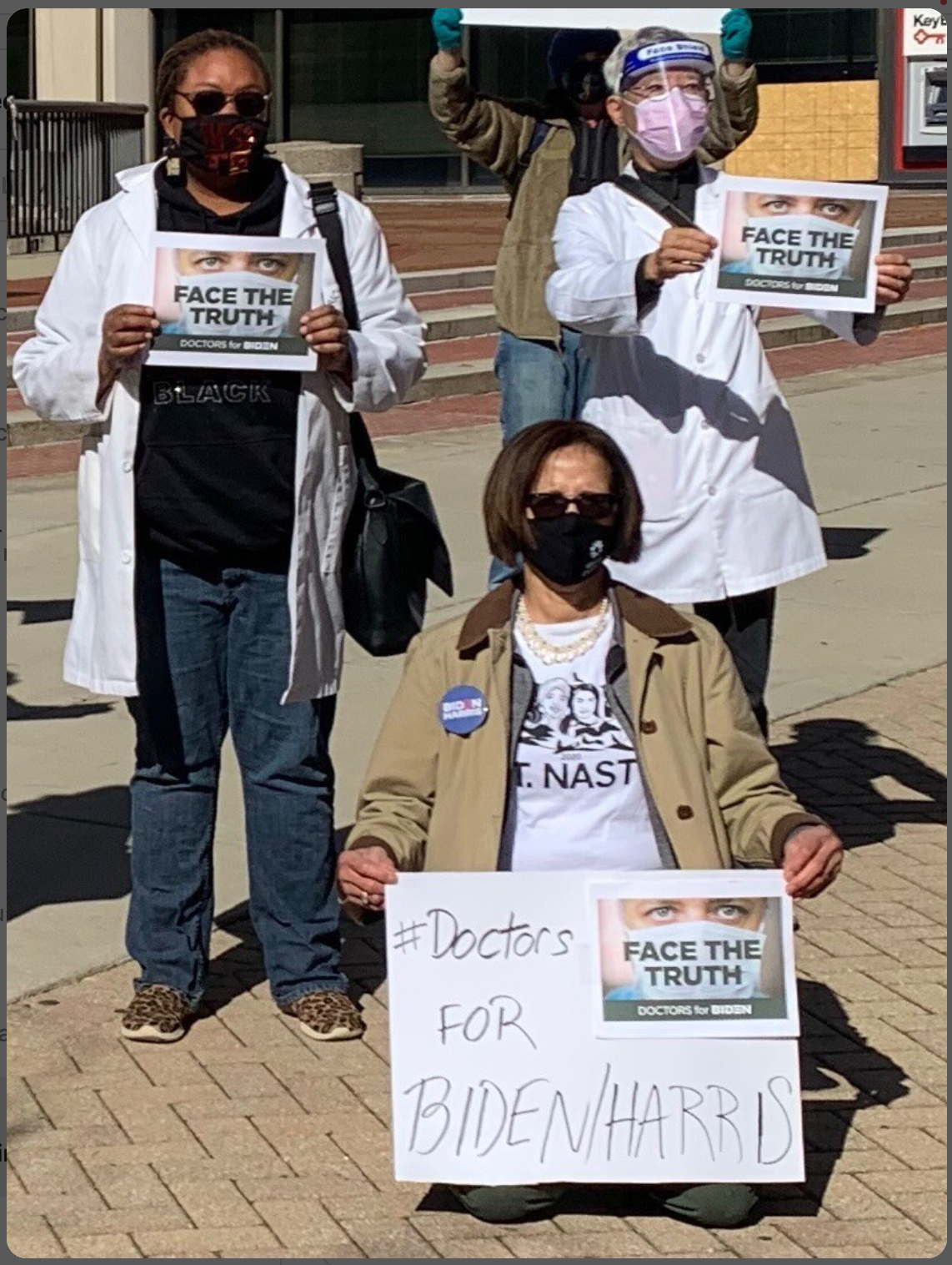 Three people in face masks and casual clothing, including a Nasty Women T-shirt, hold signs that read FACE THE TRUTH: DOCTORS FOR BIDEN, with one person holding an additional sign that says #Doctors FOR BIDEN/HARRIS.