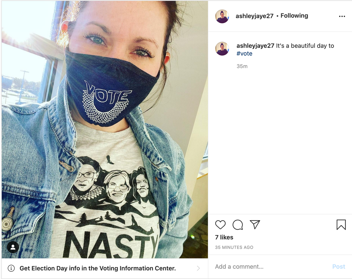 A woman wears a face mask saying VOTE above a judicial collar and a Nasty Women t-shirt featuring illustrations of Ruth Bader Ginsburg, Sonia Sotomayor, and Elena Kagan above the word NASTY.