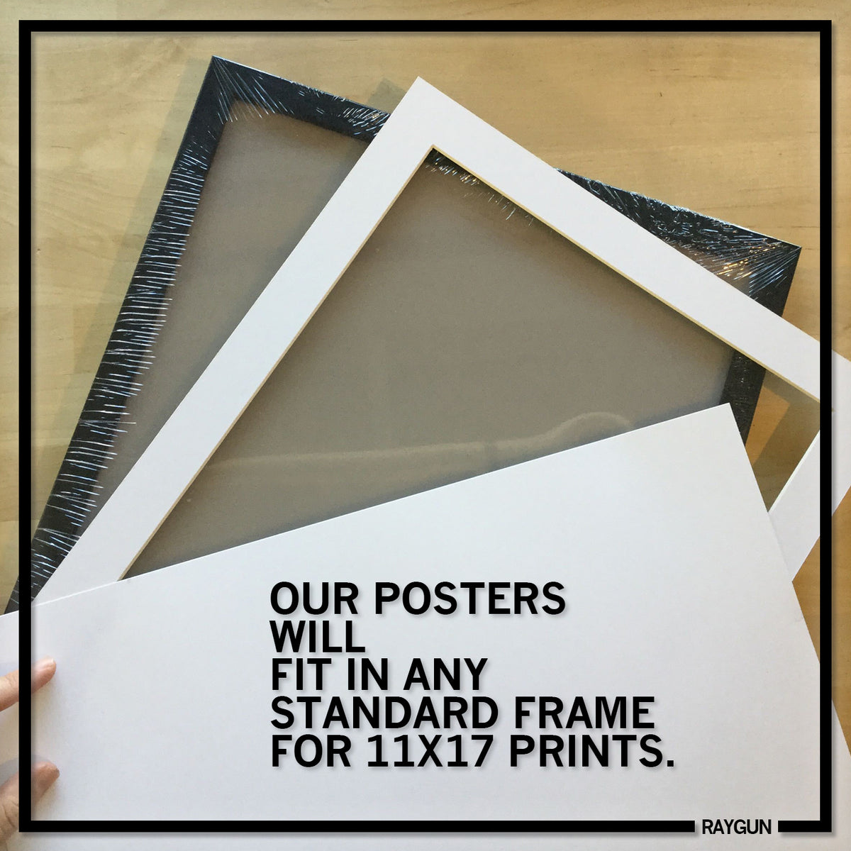 A black picture frame and a white mat board displayed on a wooden surface beside a RAYGUN poster of the Old Iowa Capitol, with text that reads: OUR POSTERS WILL FIT IN ANY STANDARD FRAME FOR 11X17 PRINTS.