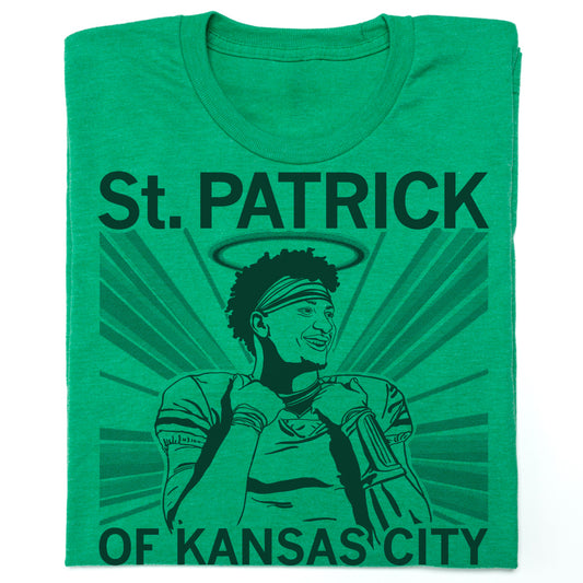 Folded heather kelly green shirt with dark ink print that reads "Saint&nbsp;Patrick of Kansas City: Restorer of Humanity, Saver of Chiefs, Great Smile." with an illustration of Patrick Mahomes with a halo over his head.