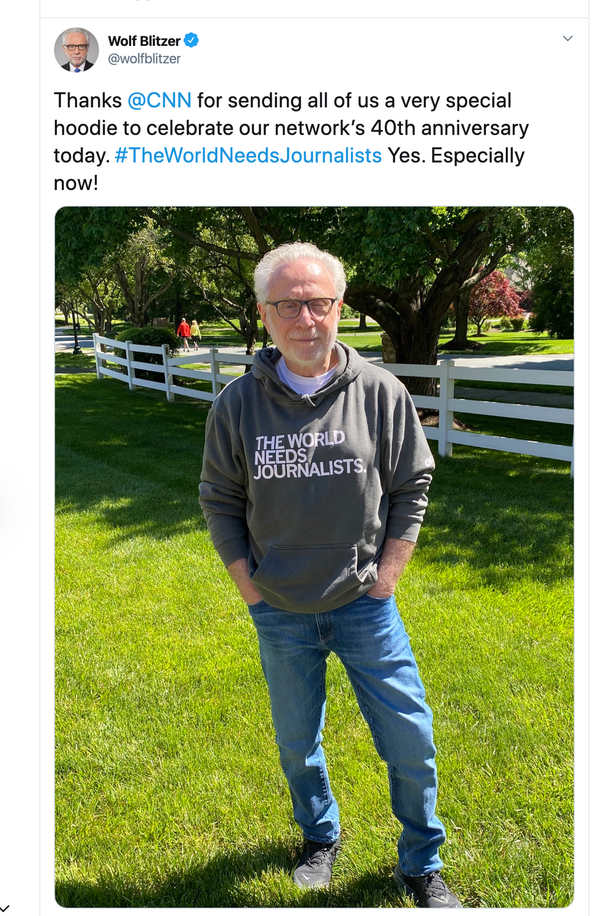 Wolf Blitzer stands outdoors wearing a gray union made pullover hoodie that reads THE WORLD NEEDS JOURNALISTS.
