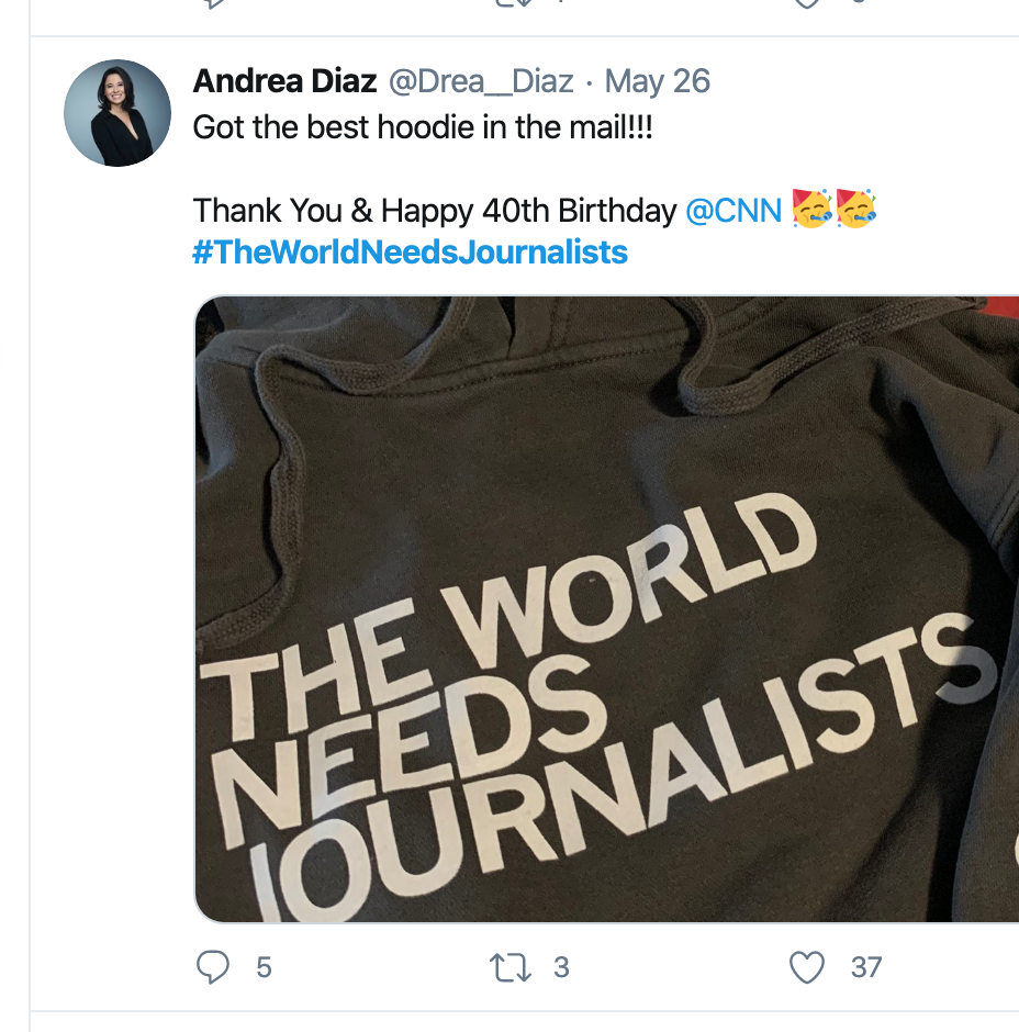 A close-up of a union-made grey pullover hoodie with the text THE WORLD NEEDS JOURNALISTS printed in white letters.