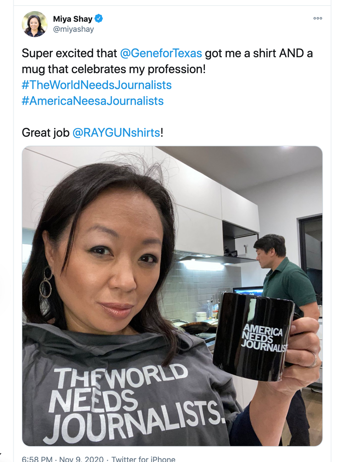 A woman in a union made grey t-shirt that says THE WORLD NEEDS JOURNALISTS holds a black mug that reads AMERICA NEEDS JOURNALISTS.
