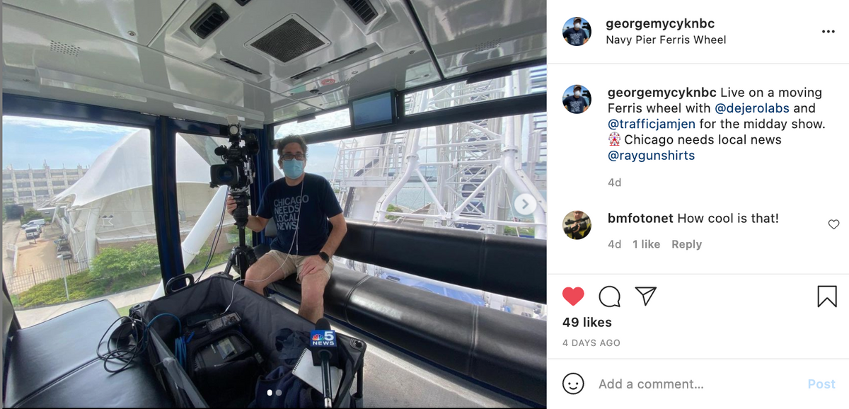 A man wearing a mask and a Block Club Chicago t-shirt operates a television camera inside a Ferris wheel gondola.