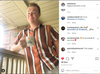 A young man in a striped button-down shirt stands on a porch holding a fade resistant Rainbow Time mug that says, Its rainbow time, bitch!.