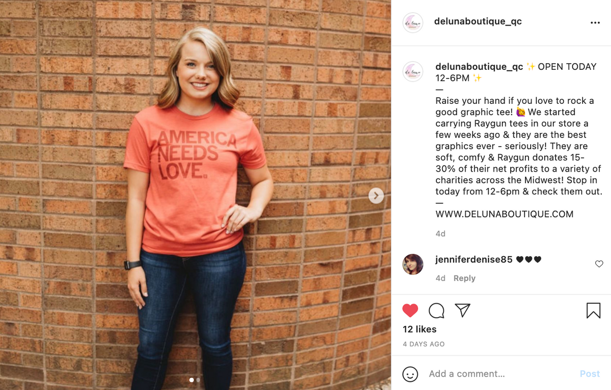 A woman wearing a heather red t-shirt that says AMERICA NEEDS LOVE in maroon lettering.