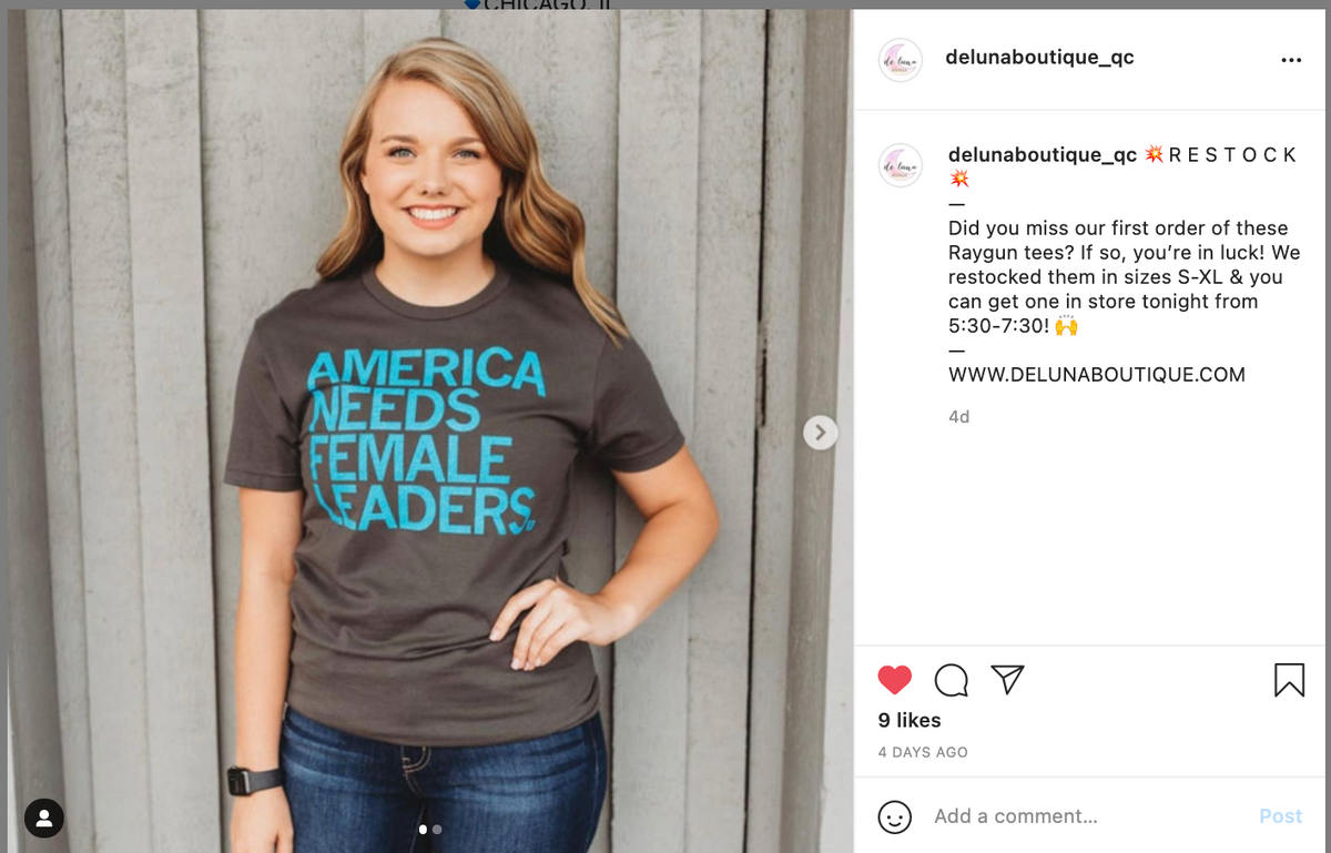 A smiling woman wearing a union made, dark gray t-shirt with the text AMERICA NEEDS FEMALE LEADERS in light blue letters.