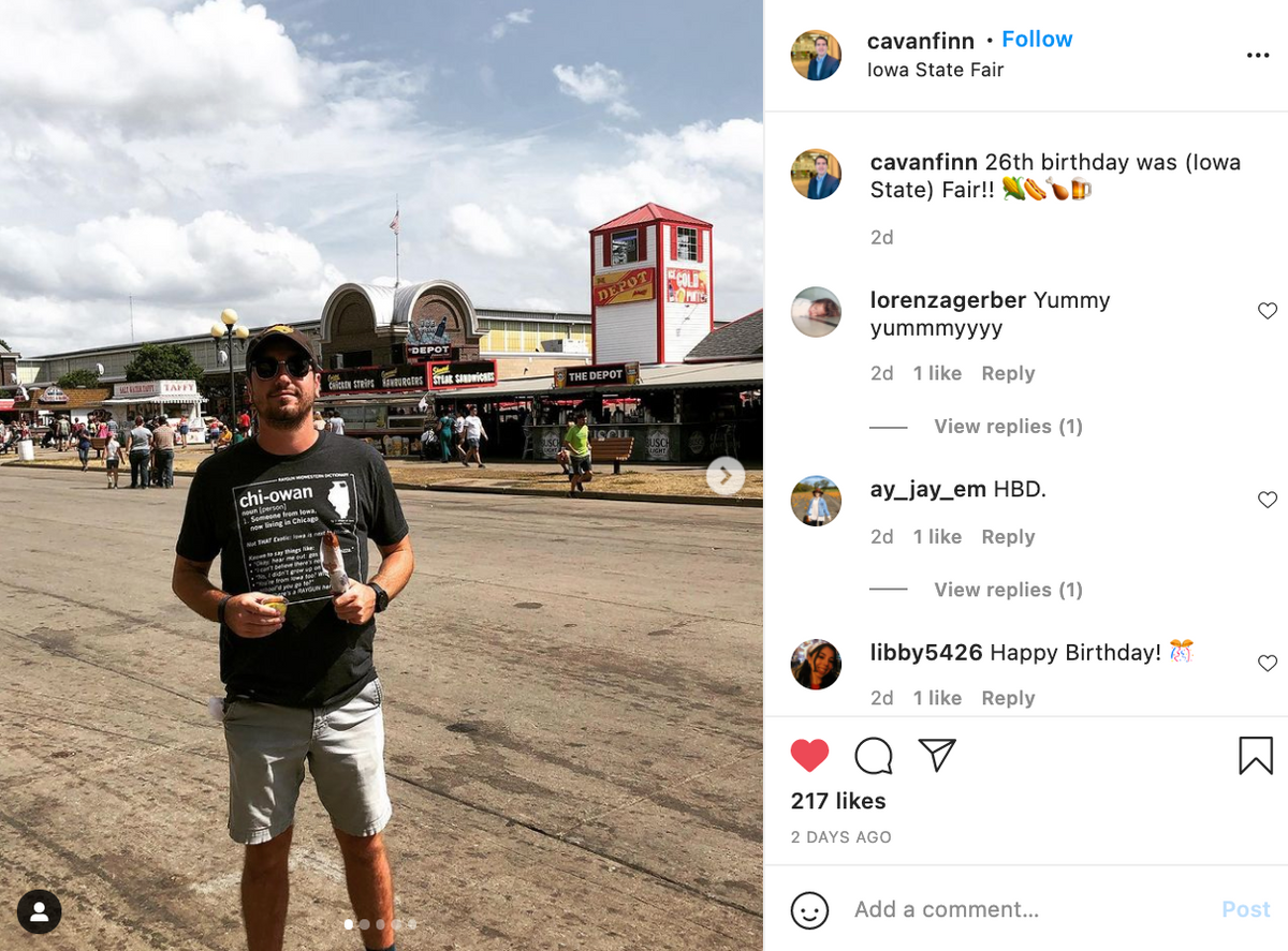 A man wearing a charcoal T-shirt that defines chi-owan stands at the Iowa State Fair in front of food stands.