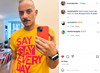 A man wearing a yellow LGBTQ+ t-shirt that says SAY GAY EVERY DAY in bold pink letters takes a mirror selfie with a red smartphone.