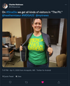 A person smiles while wearing an open blazer over a heather kelly green t-shirt that reads AMERICA NEEDS LESBIAN FARMERS.