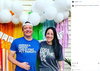 A man in a union made blue t-shirt and a woman in a grey t-shirt stand in front of a rainbow streamer backdrop decorated with white balloons and a Happy Birthday banner.