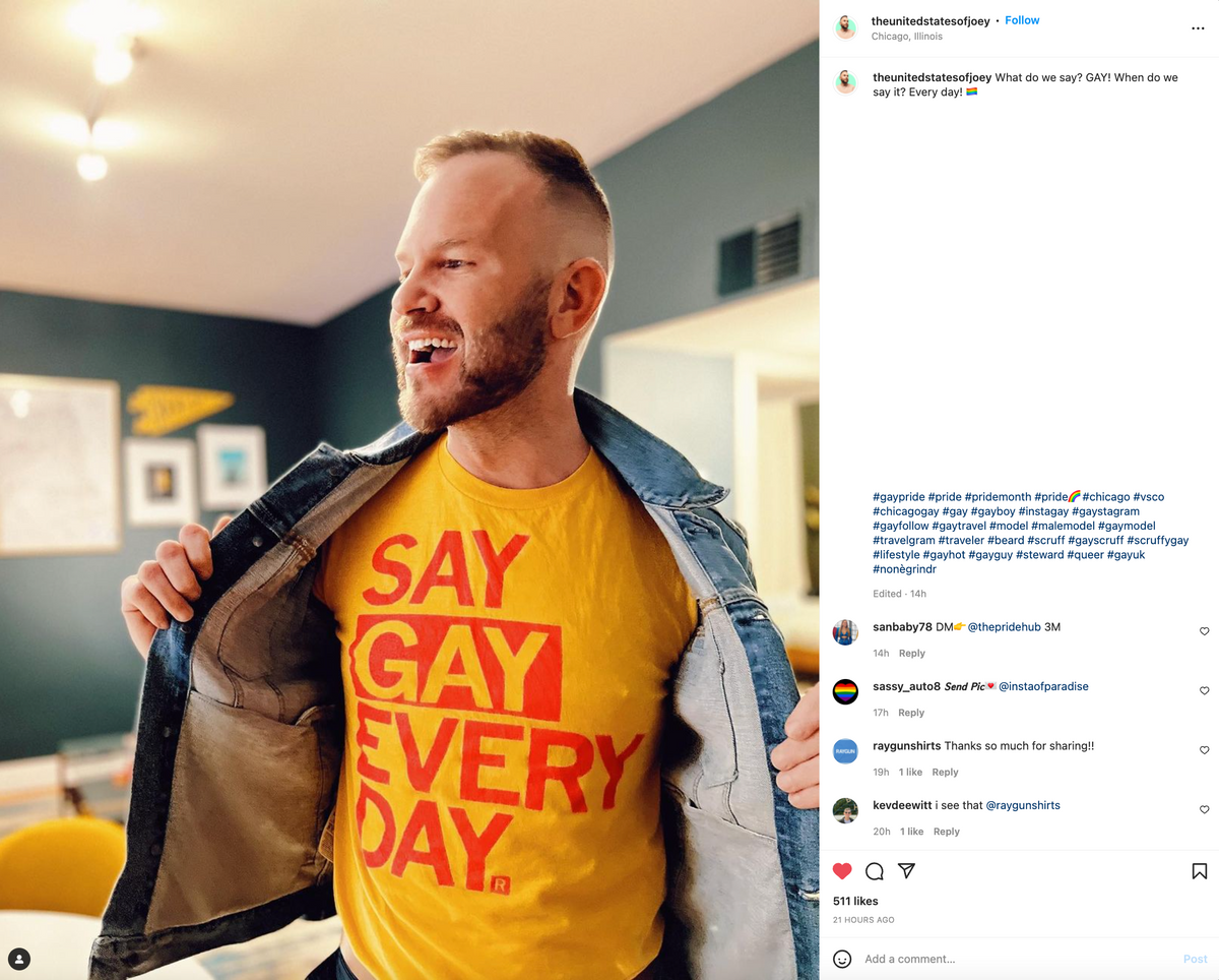 A man wearing supportive pride apparel in the form of a yellow t-shirt that says SAY GAY EVERY DAY in red block letters, with a denim jacket draped over his shoulders.