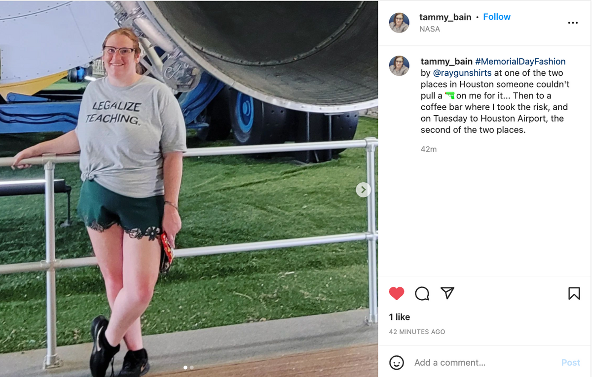 A woman smiling while leaning against a railing in front of a large aircraft engine, wearing a heather grey t-shirt that says LEGALIZE TEACHING.