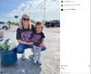 A woman and a young child crouch outdoors wearing matching black T-shirts that say Power Is The New Pretty in pink letters.