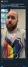 A bearded man wears a union printed grey t-shirt featuring a Progress Pride flag design.